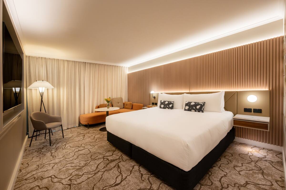 Ein Hotelzimmer mit einem großen Bett, einer Couch, einem Sessel, einem kleinen Tisch und einer Lampe.
