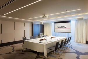 A conference room with a long table, chairs, a projector screen, and a large window with curtains.