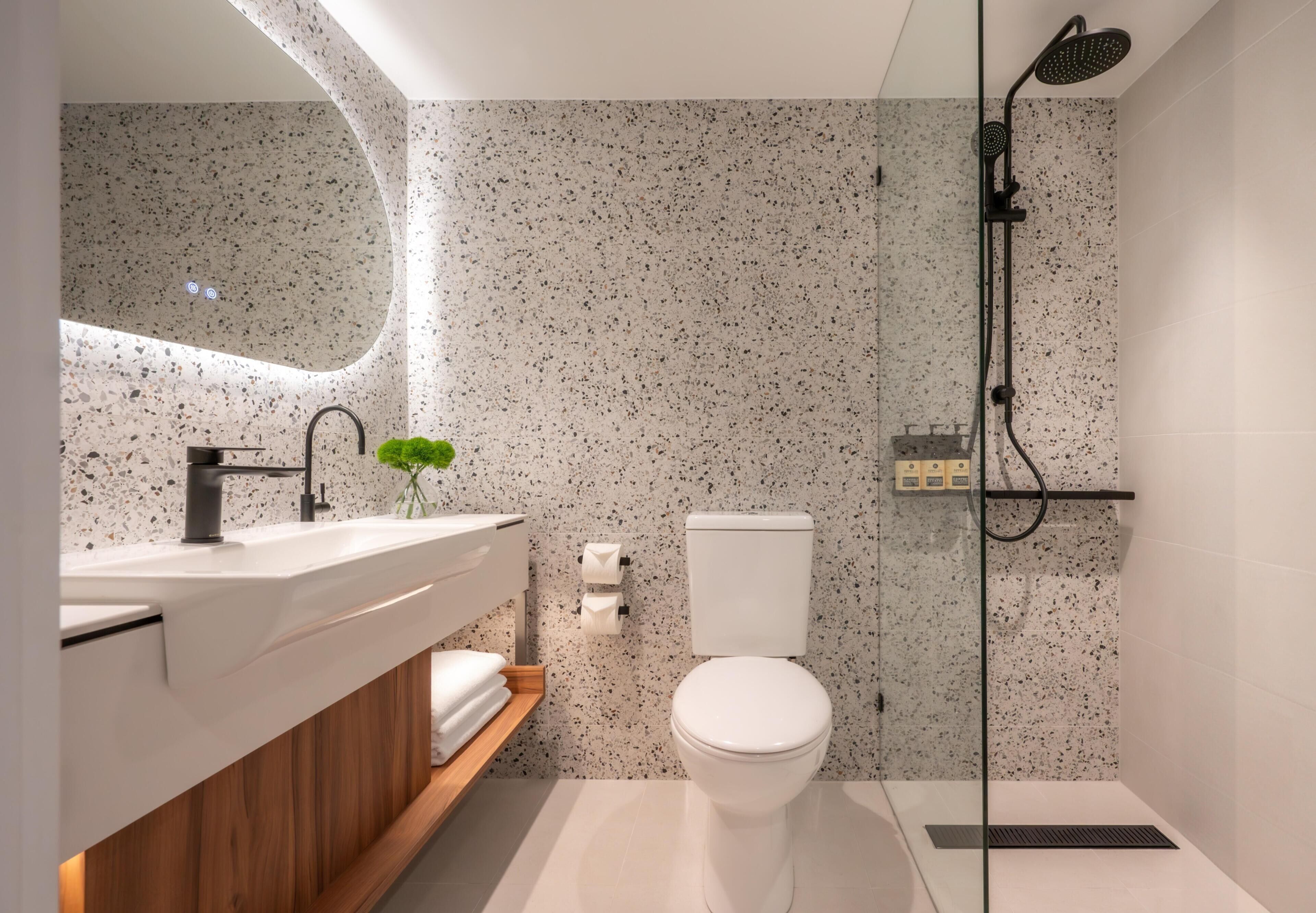 Un baño moderno con inodoro independiente, ducha con mampara de vidrio y tocador con lavabo y espejo.