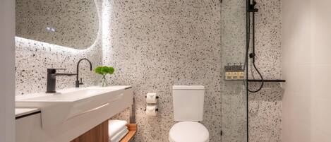 Un baño moderno con inodoro independiente, ducha con mampara de vidrio y tocador con lavabo y espejo.