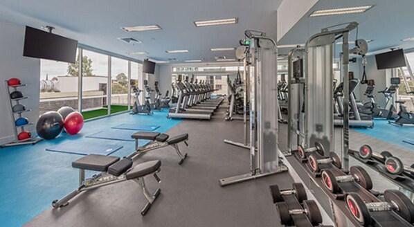 Un gimnasio con cintas de correr, máquinas de pesas y pesas libres.