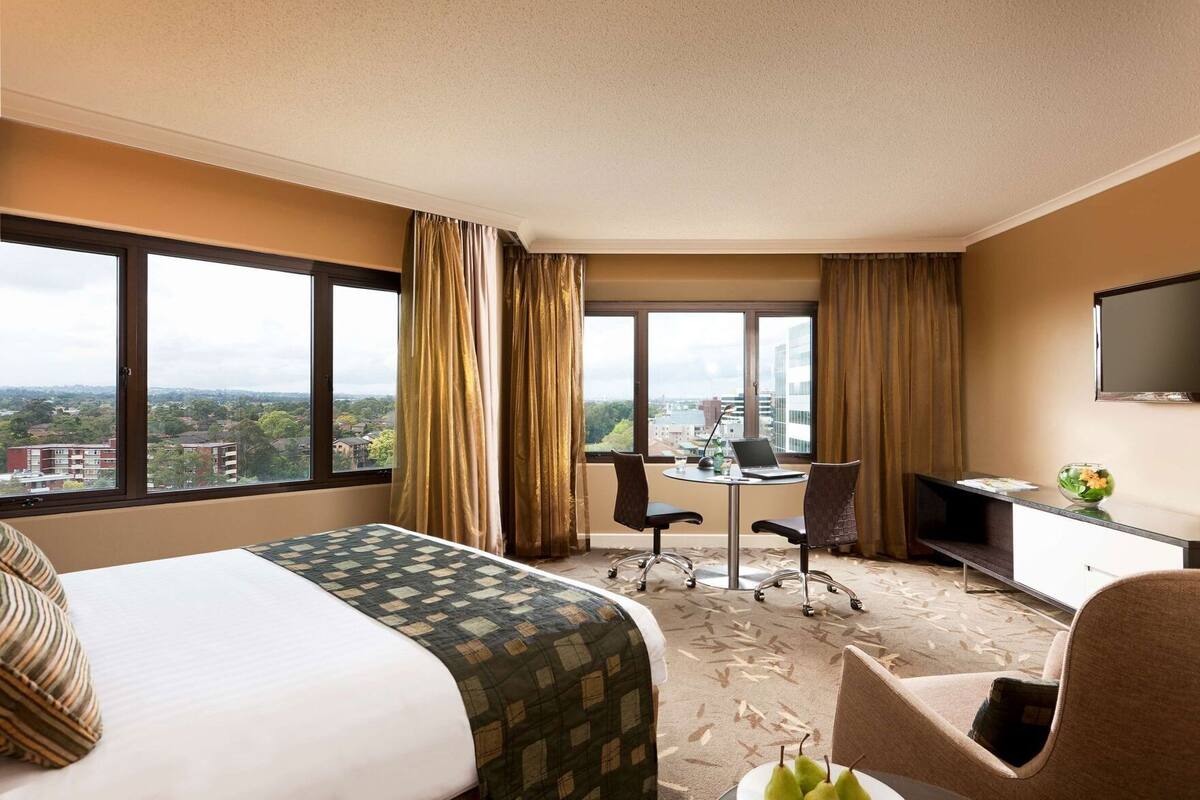 Ein Hotelzimmer mit Bett, Schreibtisch mit Laptop, Fernseher und Blick auf die Stadt.