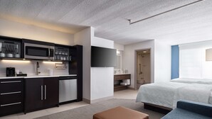 Una habitación de hotel moderna con kitchenette, una cama, un sofá y zona de ducha.