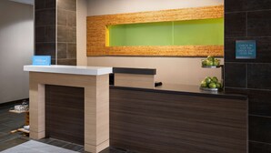 Un mostrador de recepción moderno de hotel con diseño de panel de madera, un letrero de registro de entrada/salida y una ventana verde sobre el mostrador.