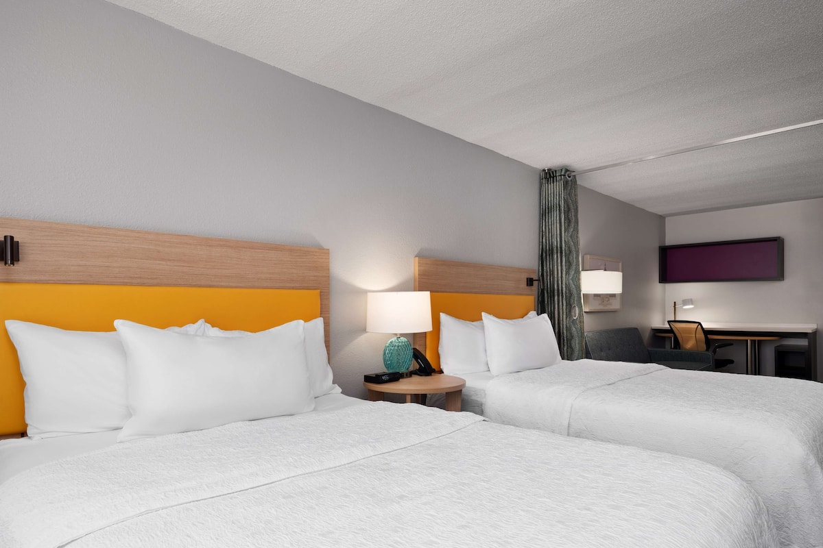 A hotel room with two beds, a desk, and a TV on the wall.