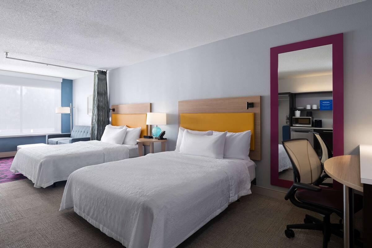 A hotel room with two beds, a desk, a chair, a TV, and a bathroom.