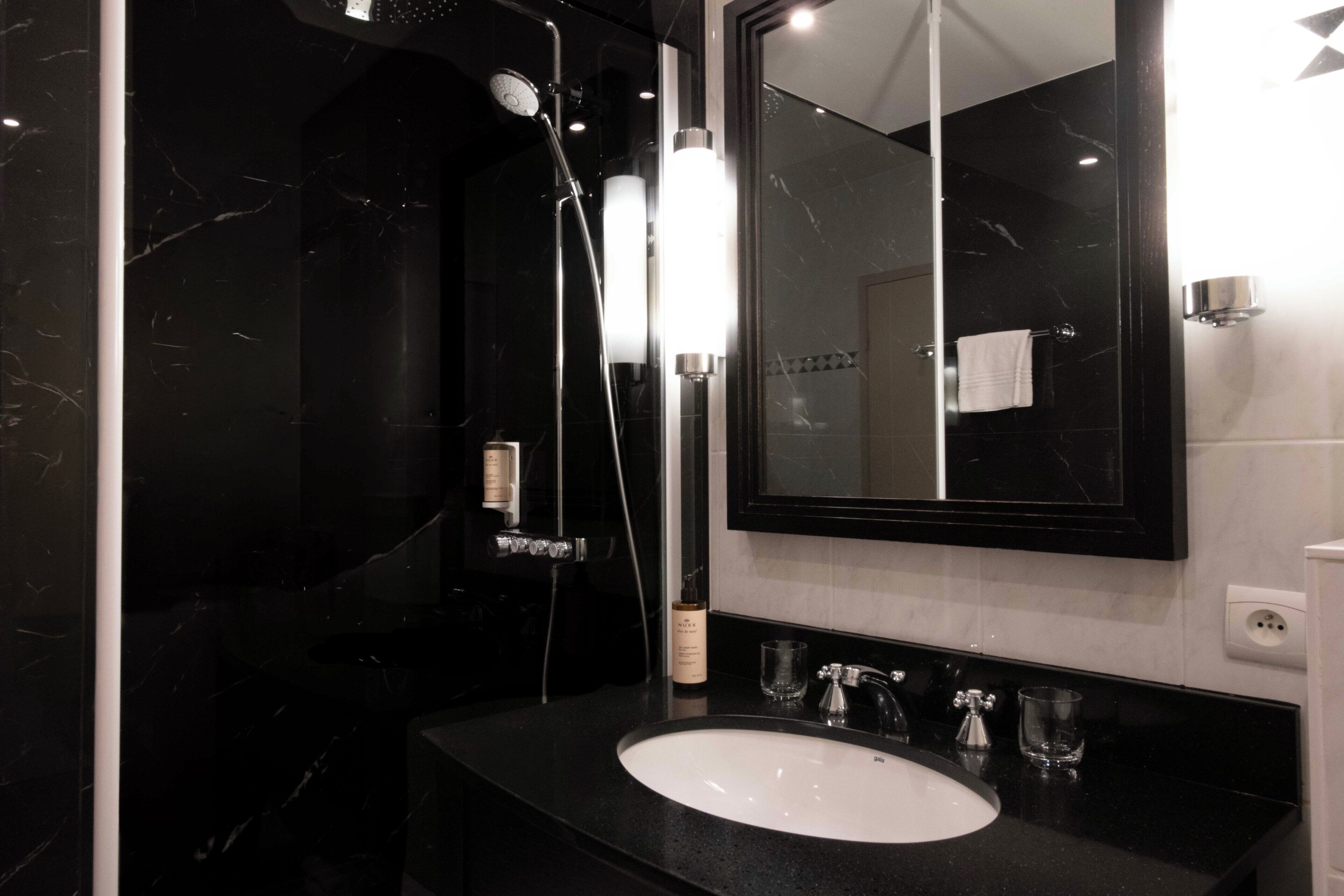 Een moderne badkamer met een zwart marmeren wastafel, een grote spiegel en een douche.
