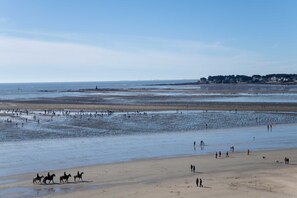 Una playa con gente caminando y jinetes a caballo.