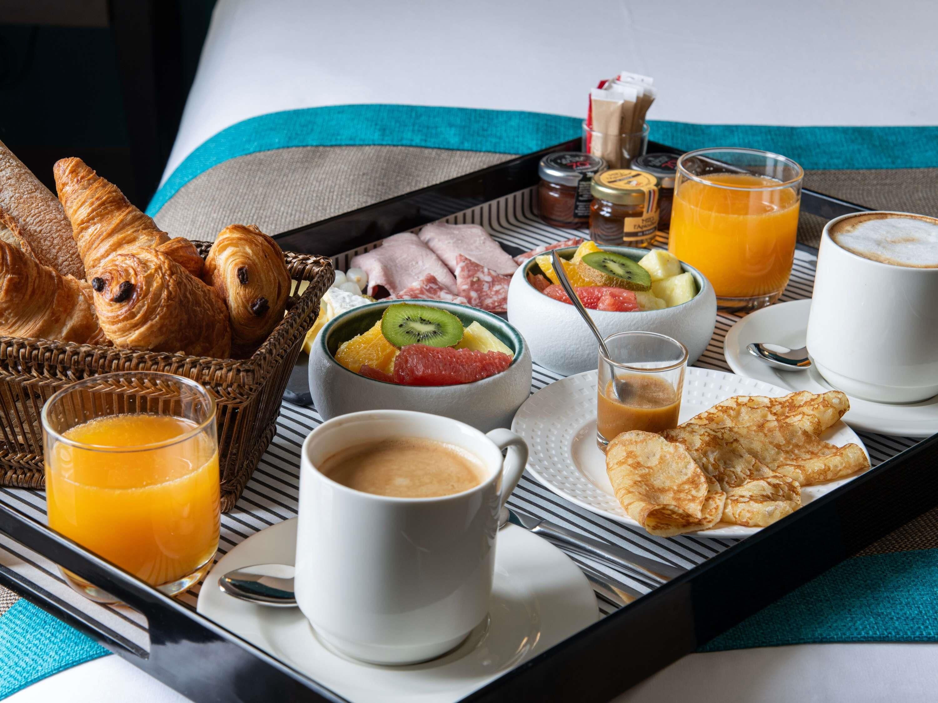 Un safata d'esmorzar amb croissants, fruita, cafè i suc de fruites.