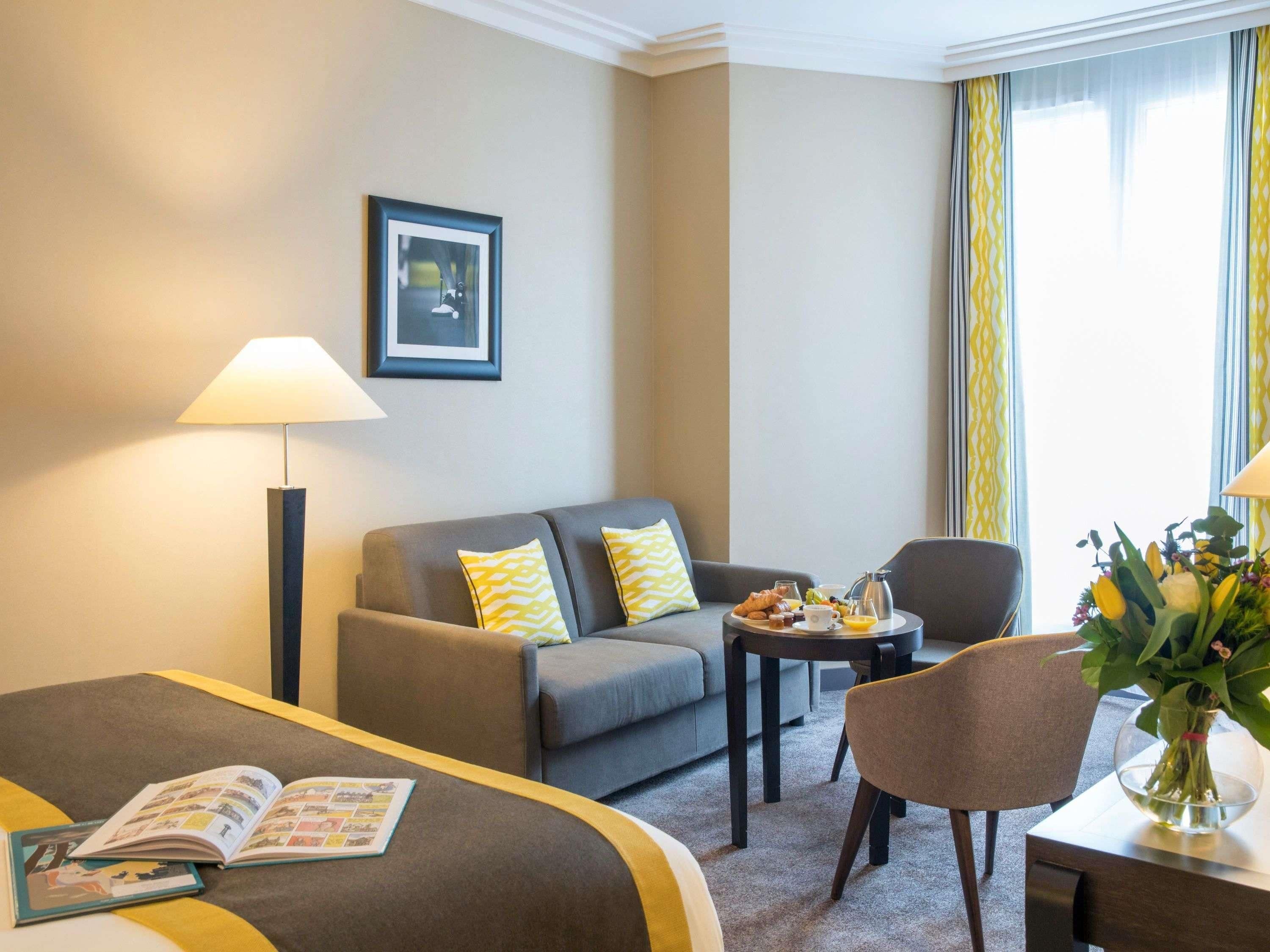Une chambre d’hôtel avec un lit, un canapé, une petite table avec un plateau de petit-déjeuner, une lampe et un tableau au mur.