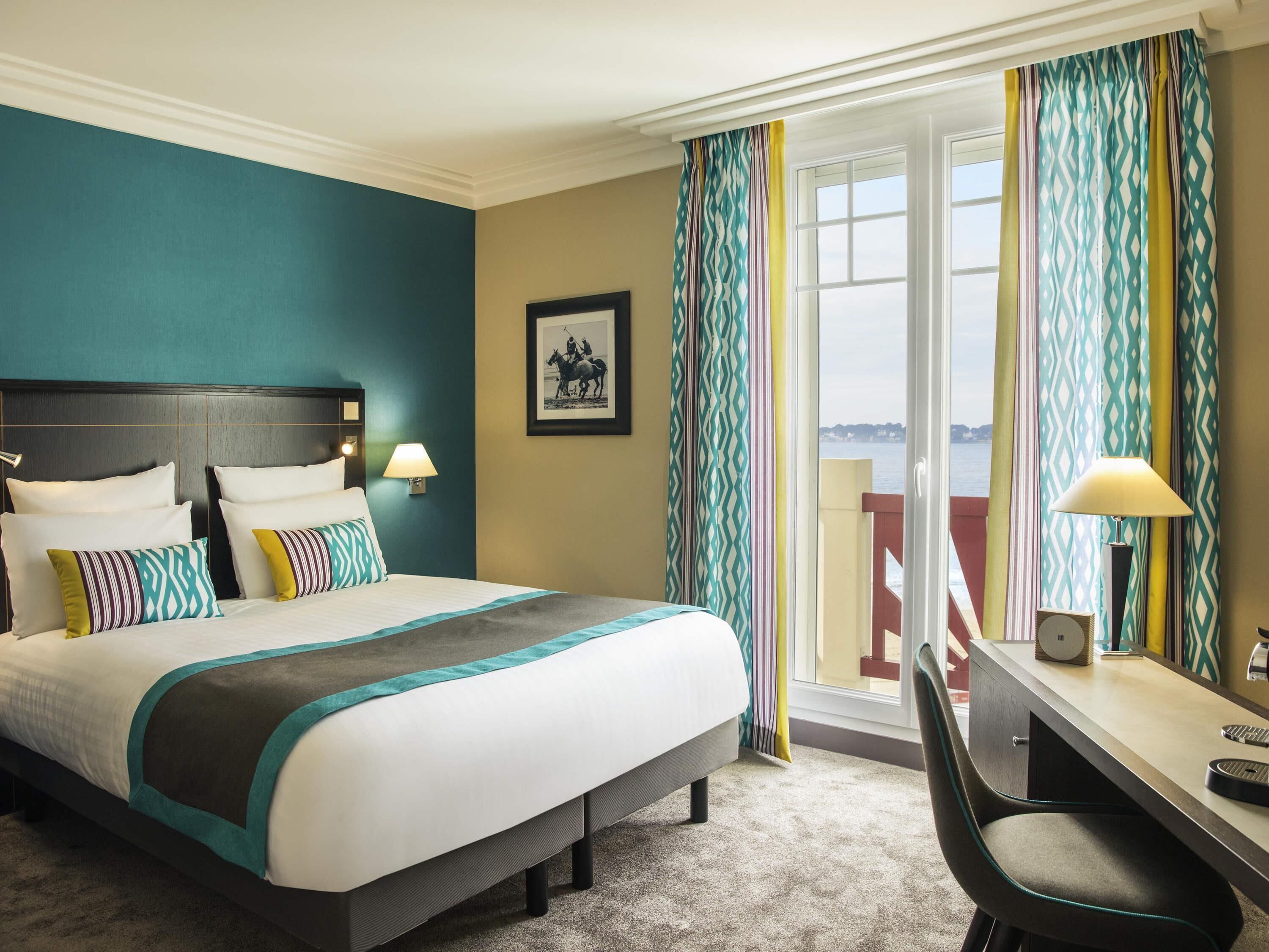 A hotel room with a bed, desk, chair, and a view of the sea.