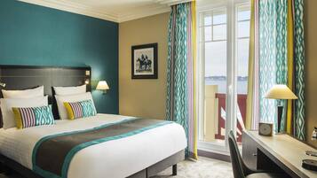 A hotel room with a bed, desk, chair, and a view of the sea.