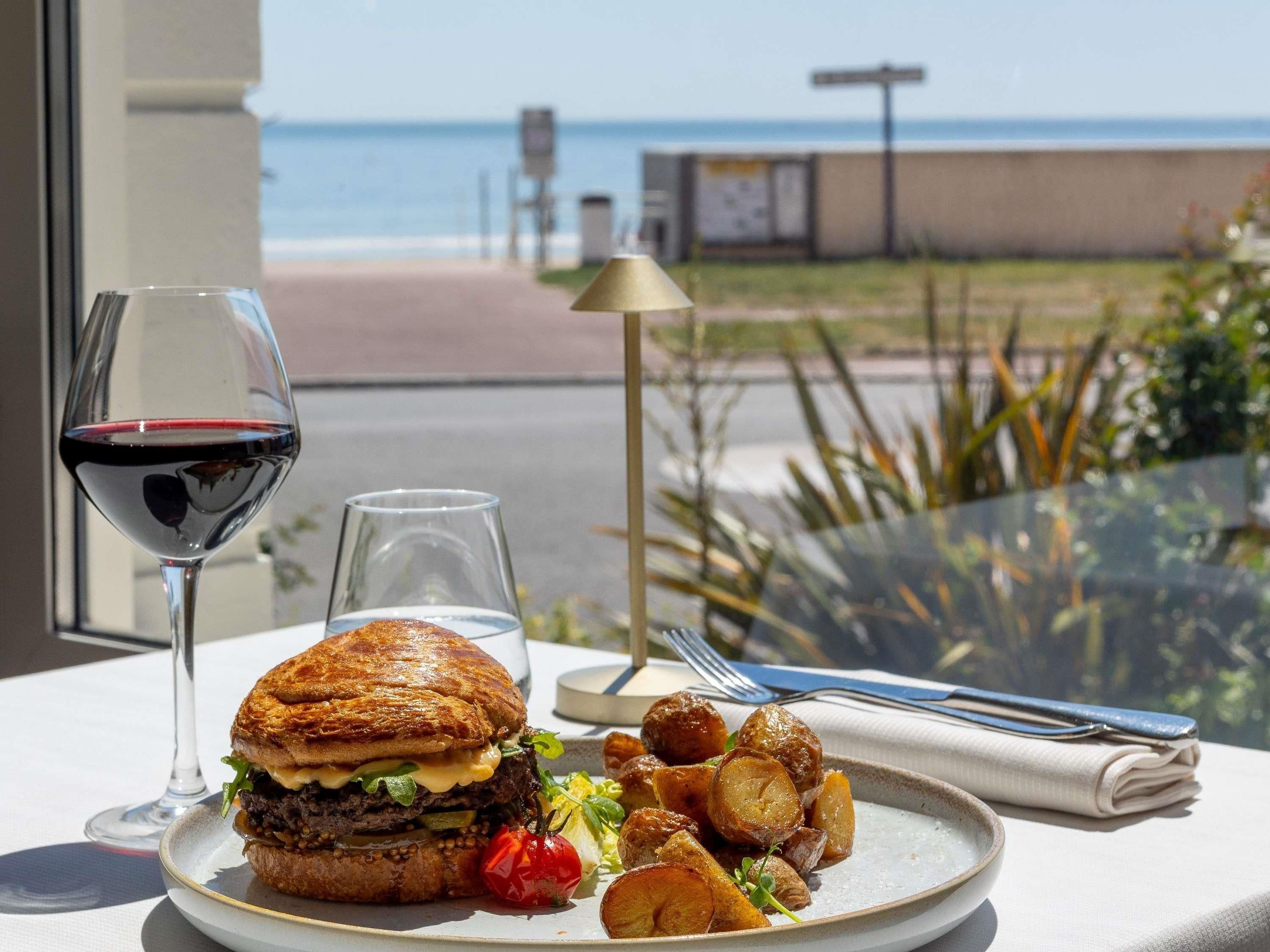 Eine Mahlzeit mit einem Hamburger, Pommes und einem Glas Rotwein auf einem Tisch mit Blick auf den Strand.