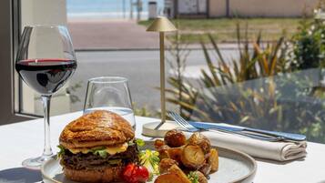 Eine Mahlzeit mit einem Hamburger, Pommes und einem Glas Rotwein auf einem Tisch mit Blick auf den Strand.