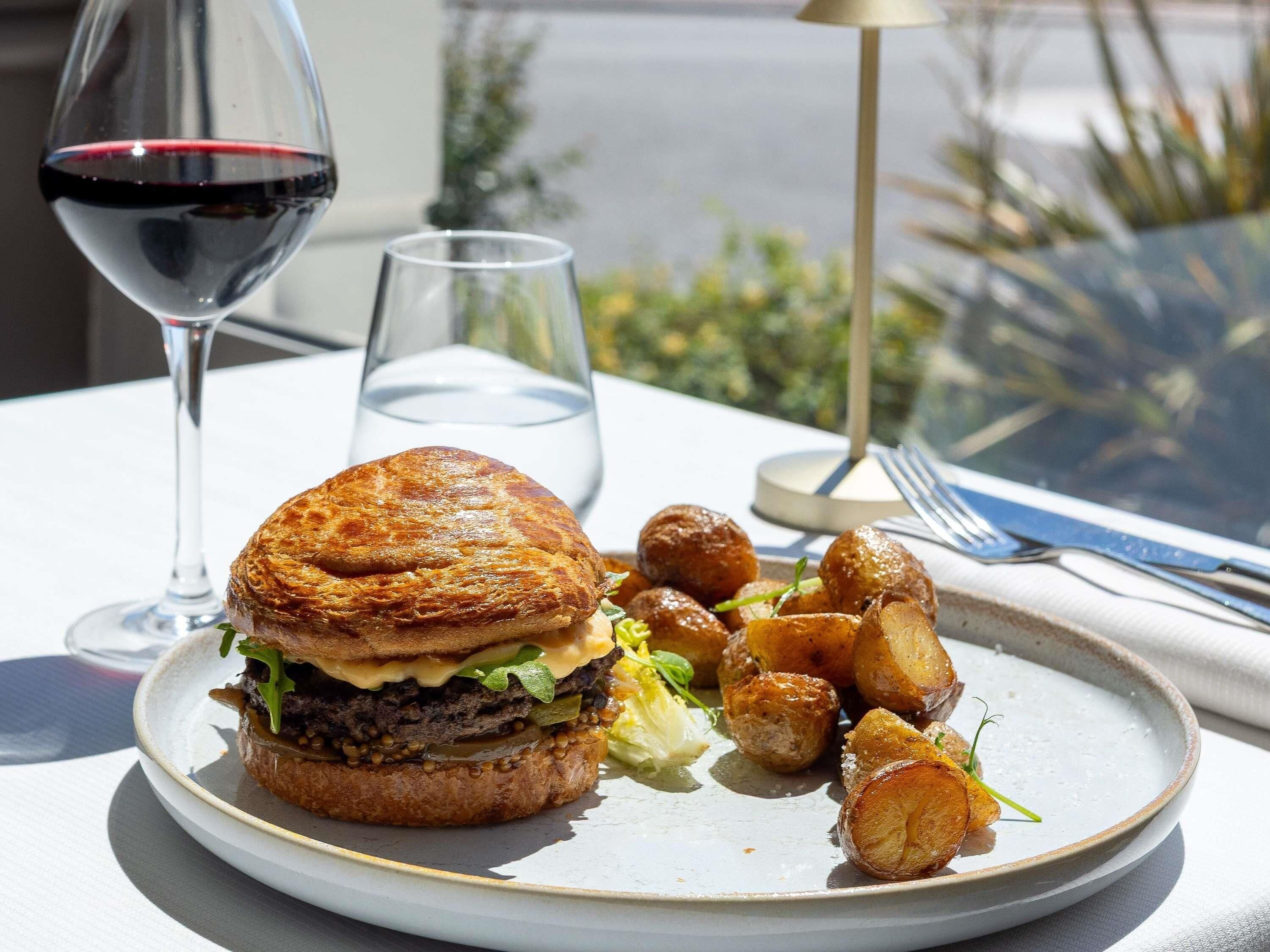 A plate with a sandwich and roasted potatoes, a glass of red wine, and a clear glass of water on a table.