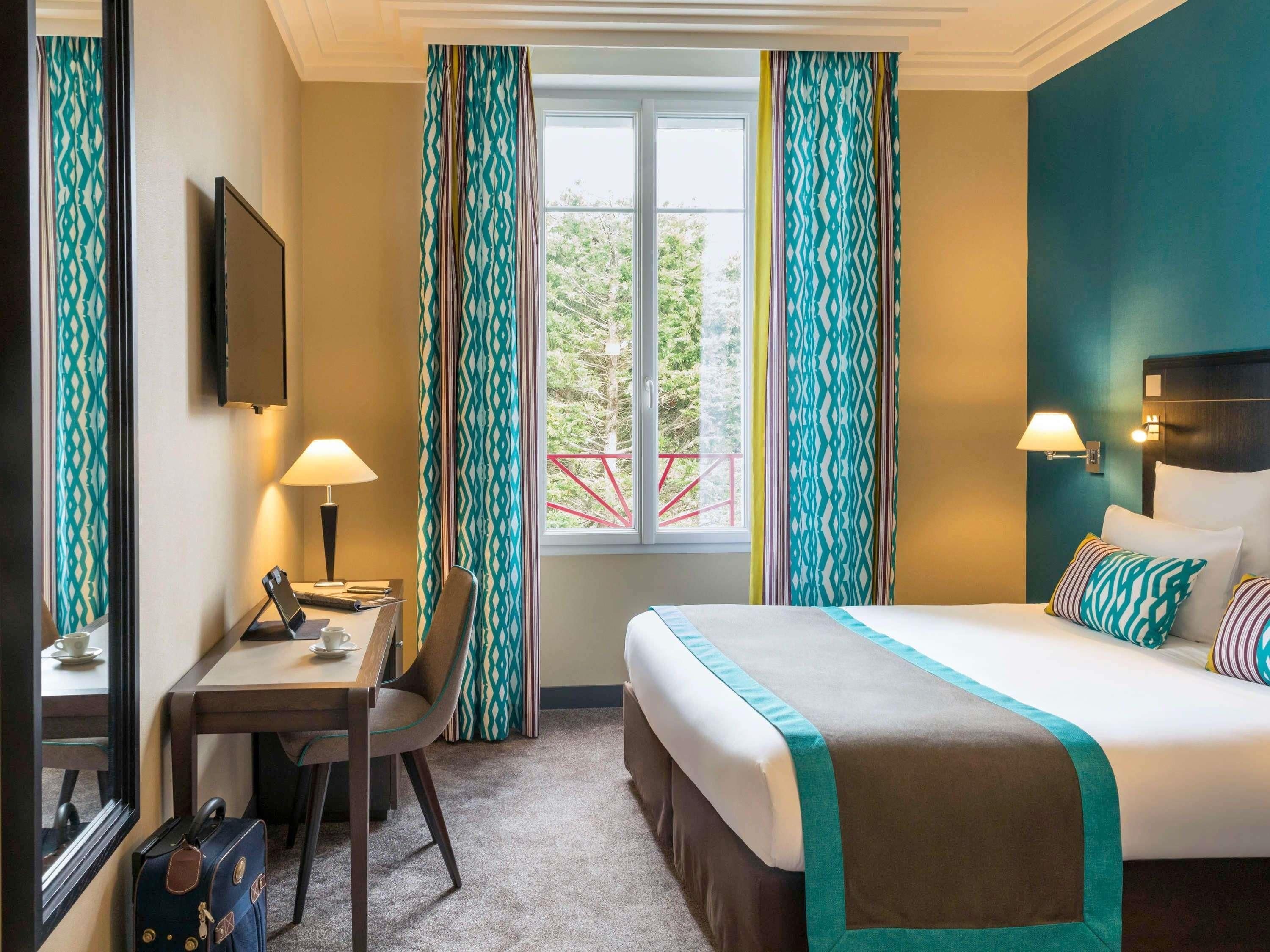 A hotel room with a bed, desk, chair, and a window with curtains.