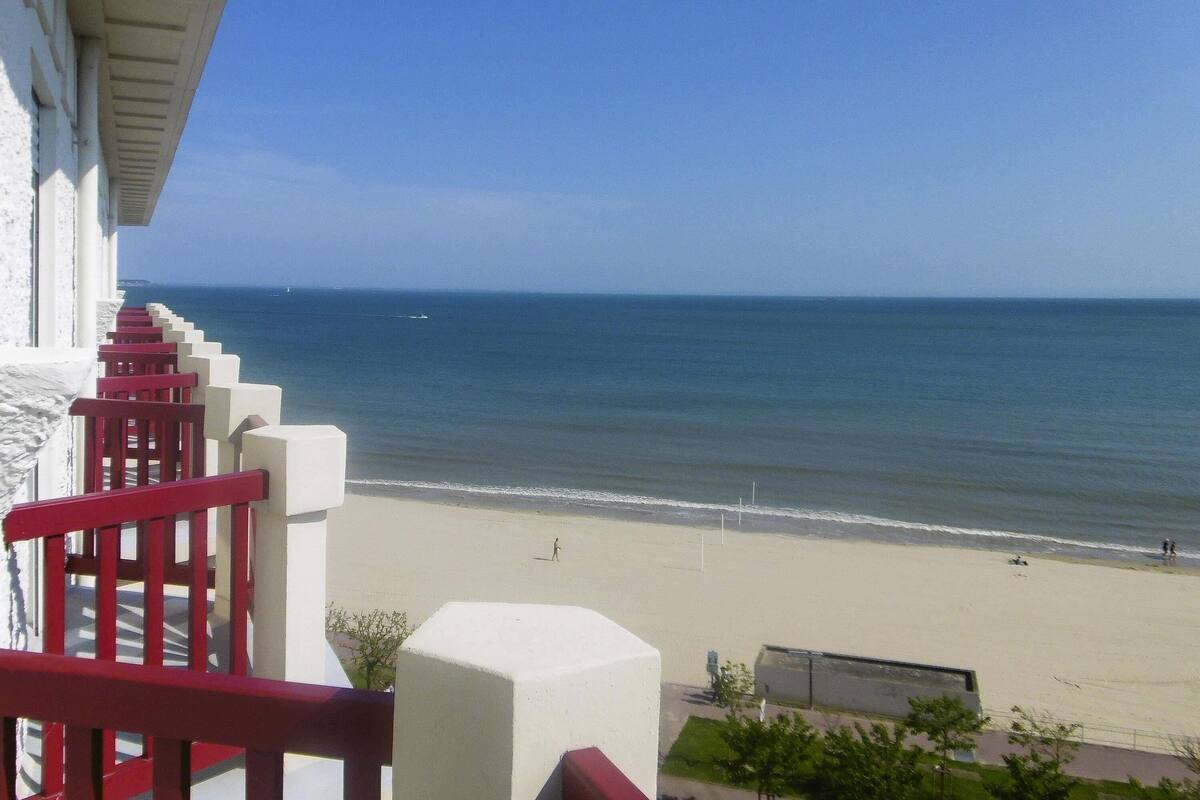 A balcony with red railings overlooking a beach with a clear view of the ocean.