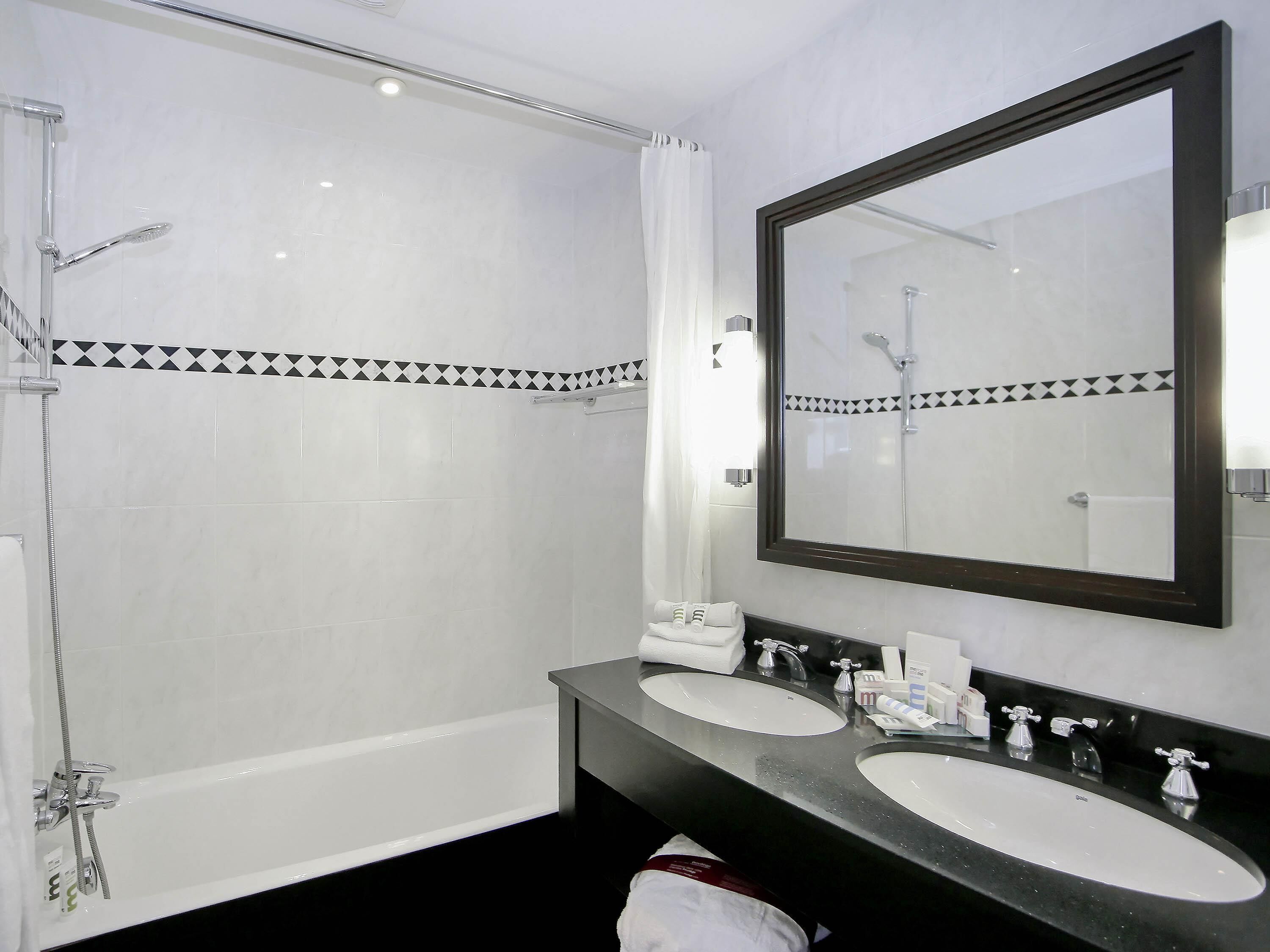 A bathroom with a shower, two sinks, a large mirror, and a towel rack.