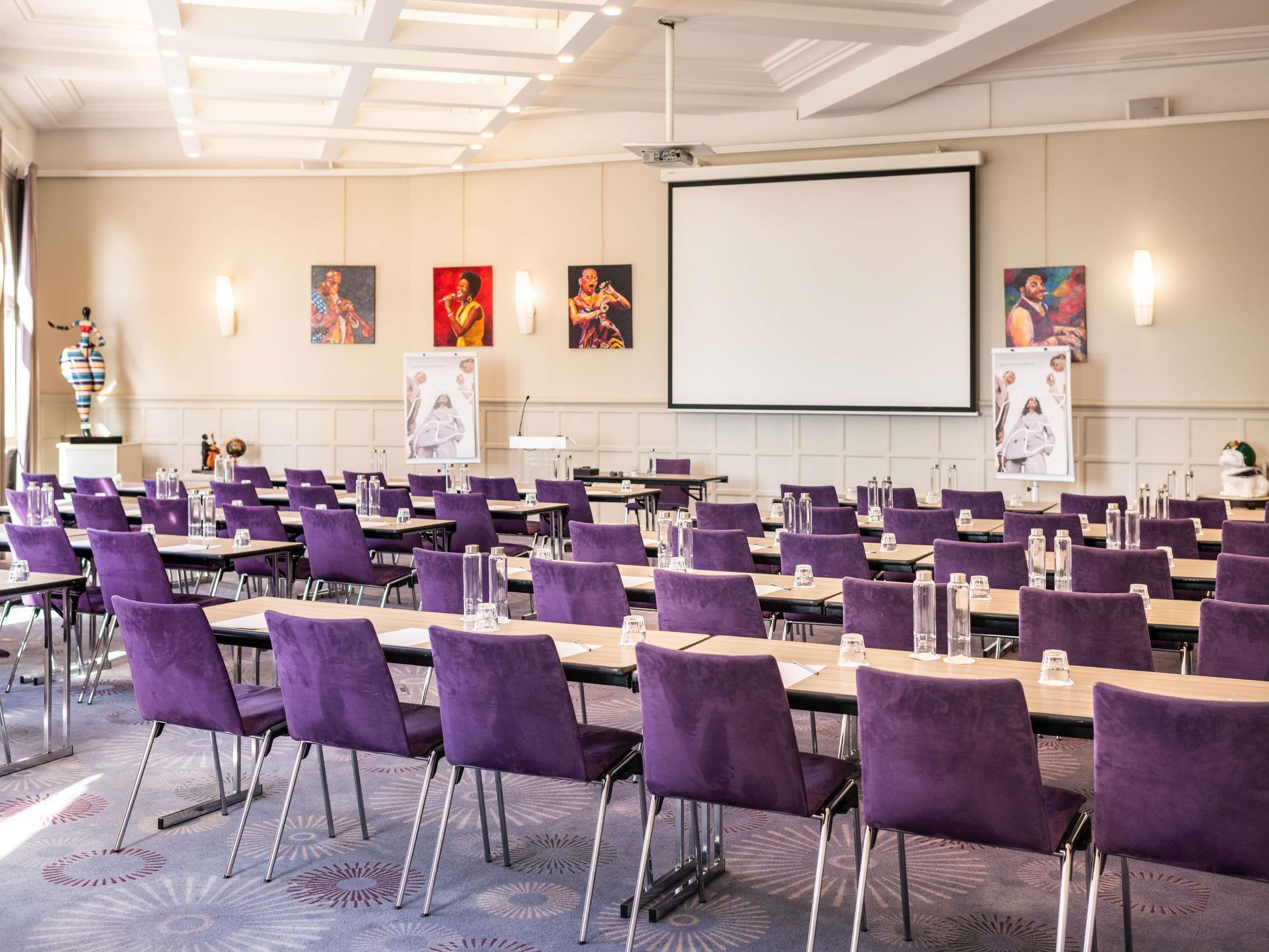 Un salón de conferencias con sillas, mesas y una pantalla grande, todo en color morado.
