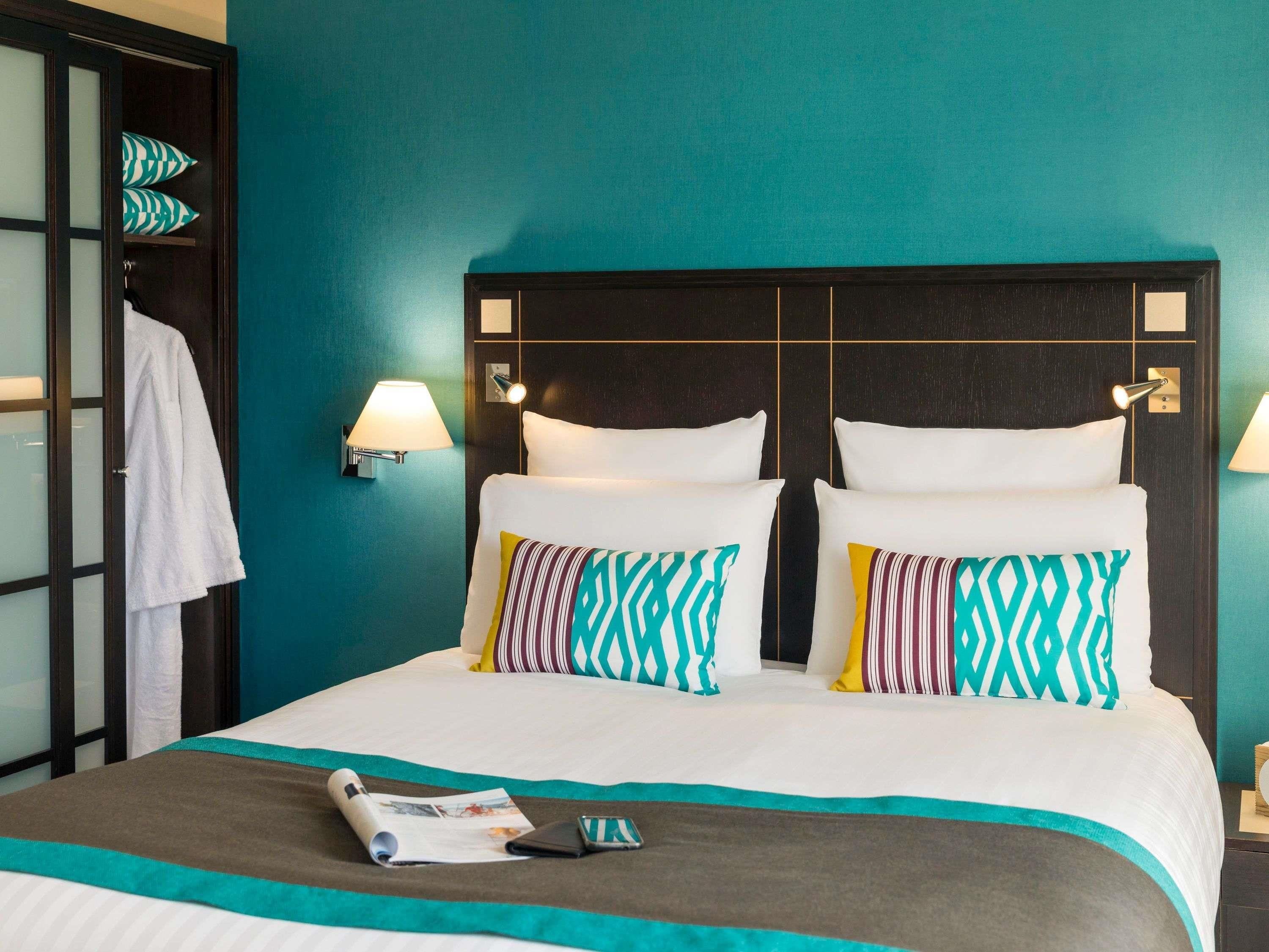 Egy szállodai szoba, amelyben egy nagy ágy, két éjjeli lámpa és egy törölközőtartó található.