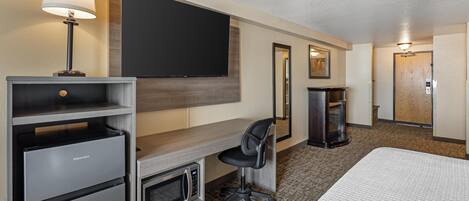 Een hotelkamer met een bed, een bureau met stoel, een televisie, een minibar en een deur.