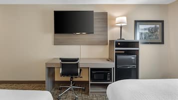 A hotel room with a desk, a flat-screen TV, a refrigerator, a lamp, and two beds.