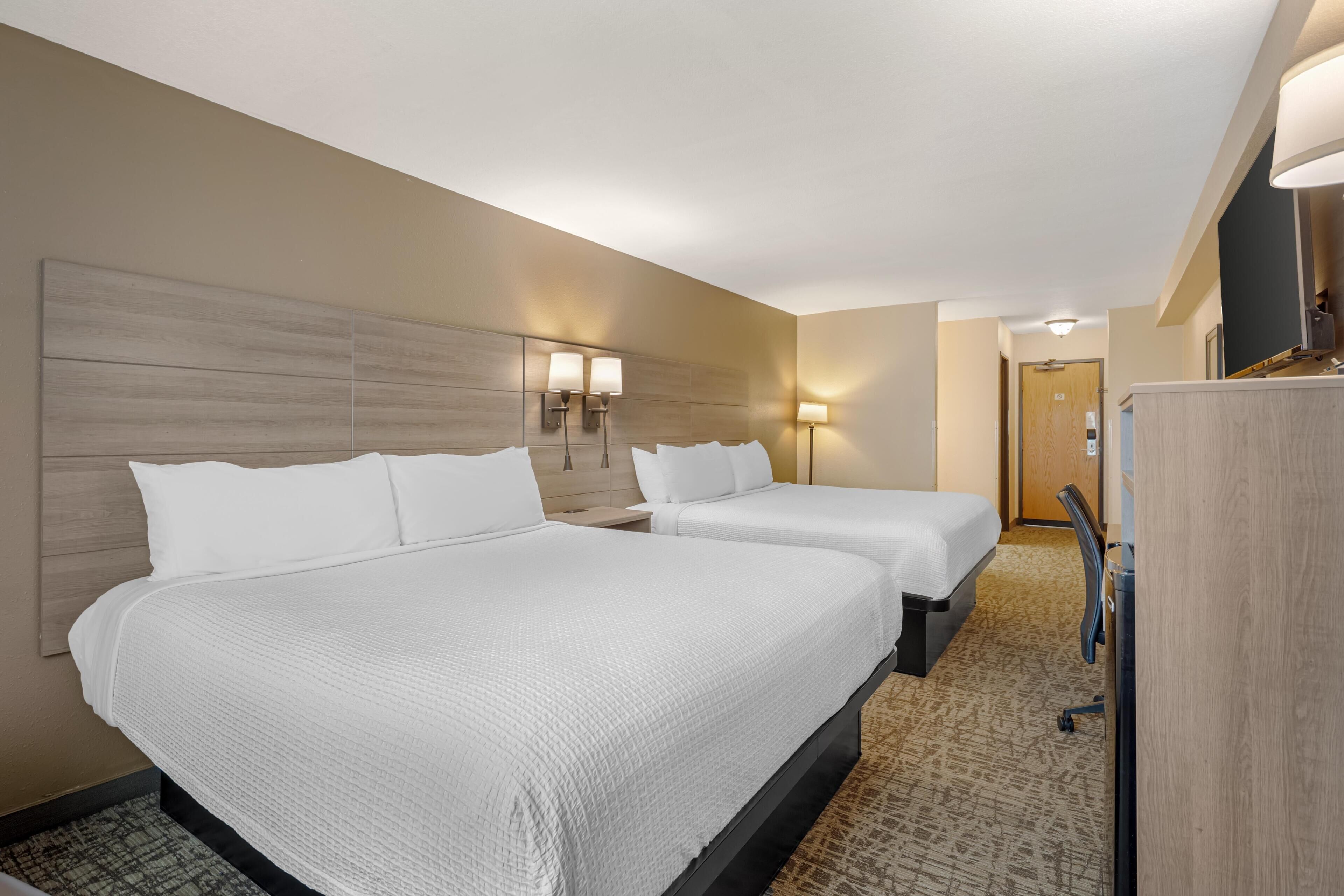 A hotel room with two beds, a wooden headboard, a desk, and a wardrobe.