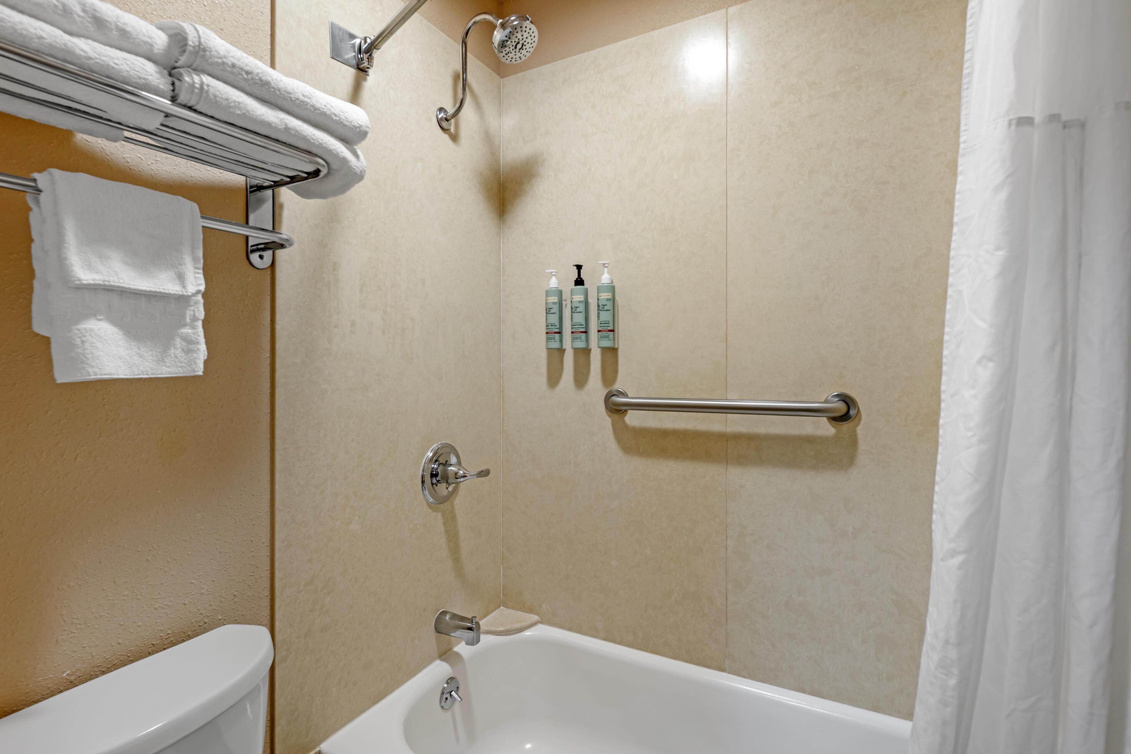 A bathroom with a bathtub, a toilet, a towel rack, and toiletries.