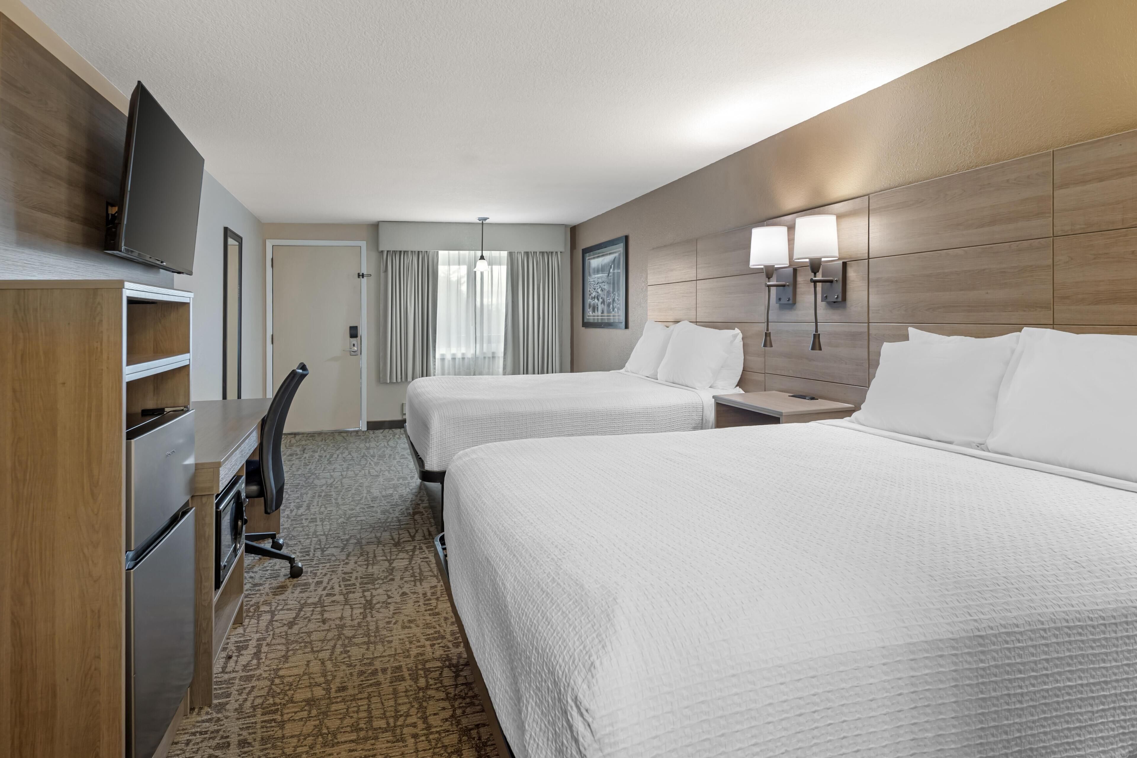 A hotel room with two beds, a desk, a chair, a television, and a window with curtains.