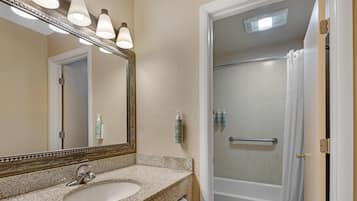 Un baño con lavamanos de encimera de granito, un espejo con iluminación, ducha con puerta de vidrio y artículos de aseo en la pared.