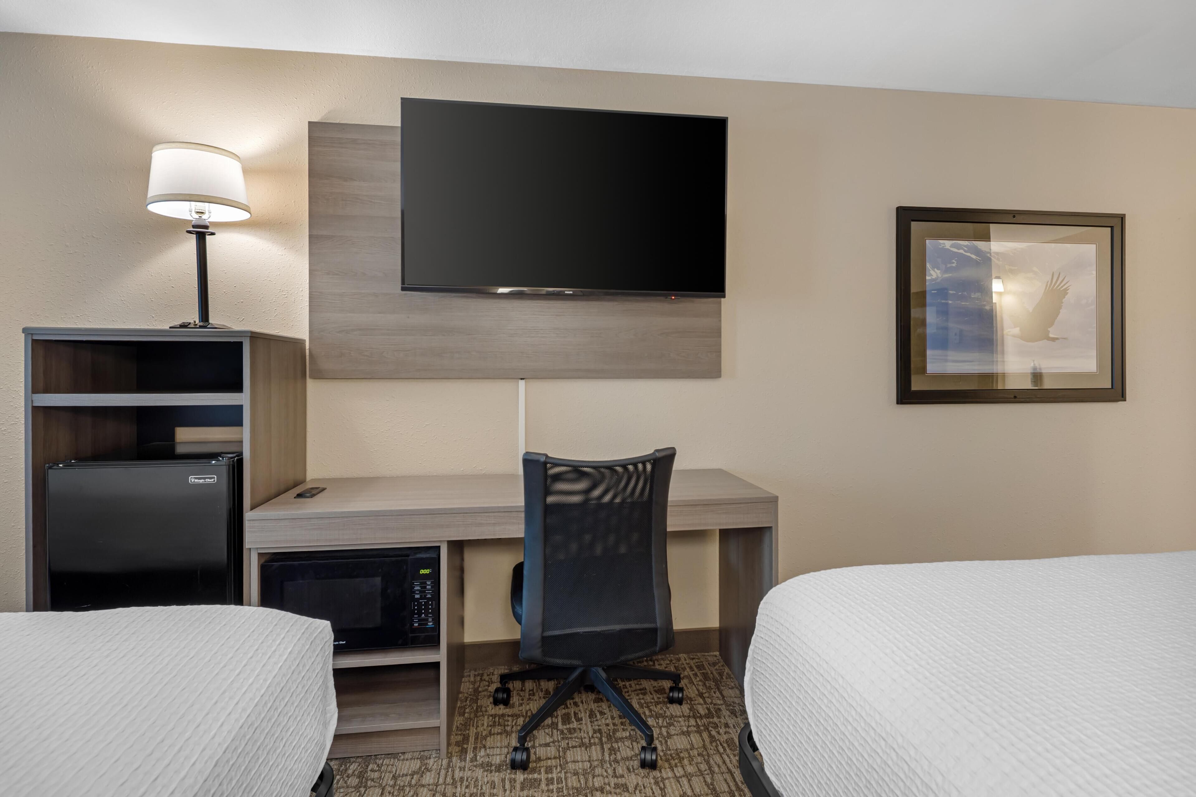 Une chambre d’hôtel avec un lit, un bureau avec un ordinateur, une télévision et une chaise.