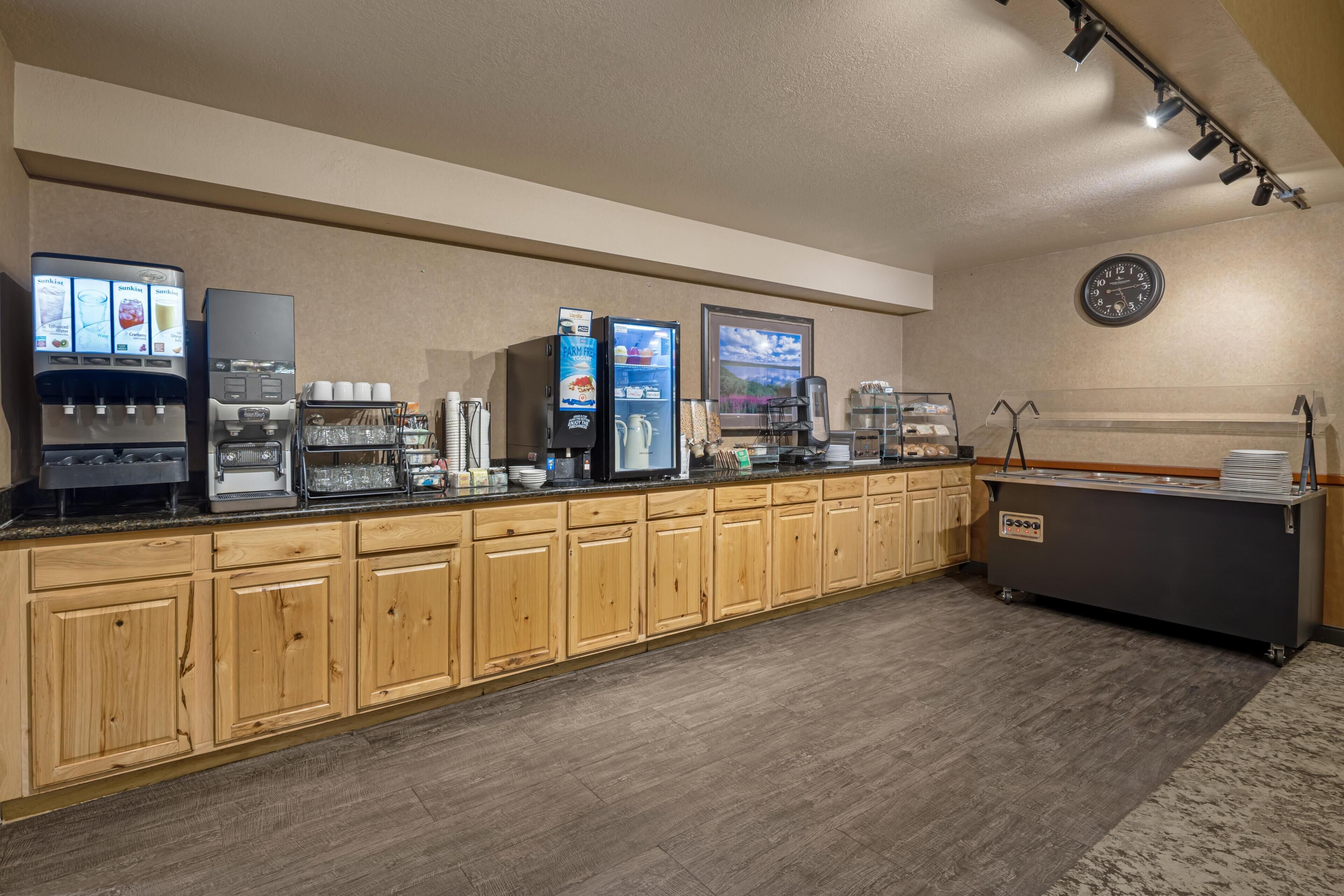 A self-service breakfast area with beverage dispensers, a refrigerator, and a coffee machine.