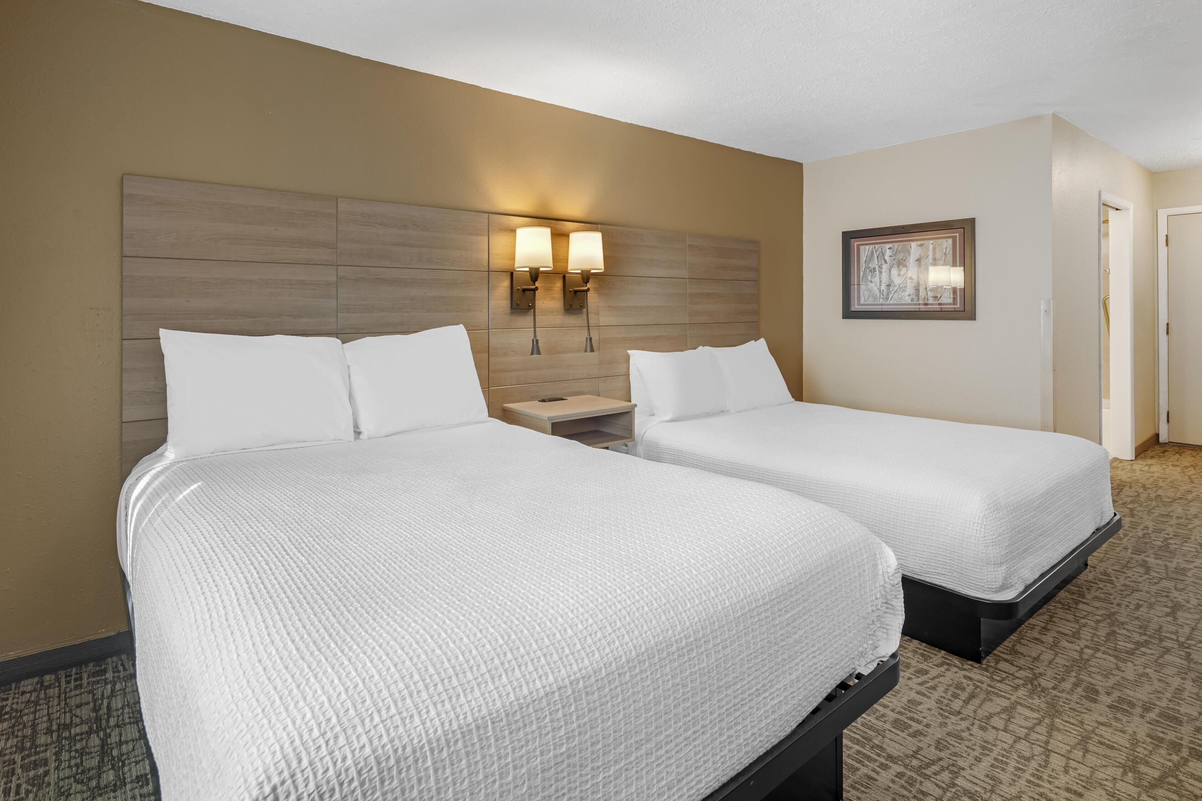 Habitación de hotel con dos camas, cabecero de madera, lámparas de pared e imagen en un marco colgada en la pared.