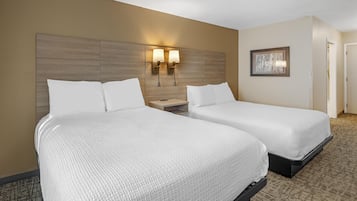 A hotel room with two beds, a wooden headboard, wall-mounted lamps, and a framed picture on the wall.