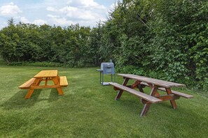 Two picnic tables in a grassy area with dense foliage in the background. - Best Western Bidarka Inn (Homer)
