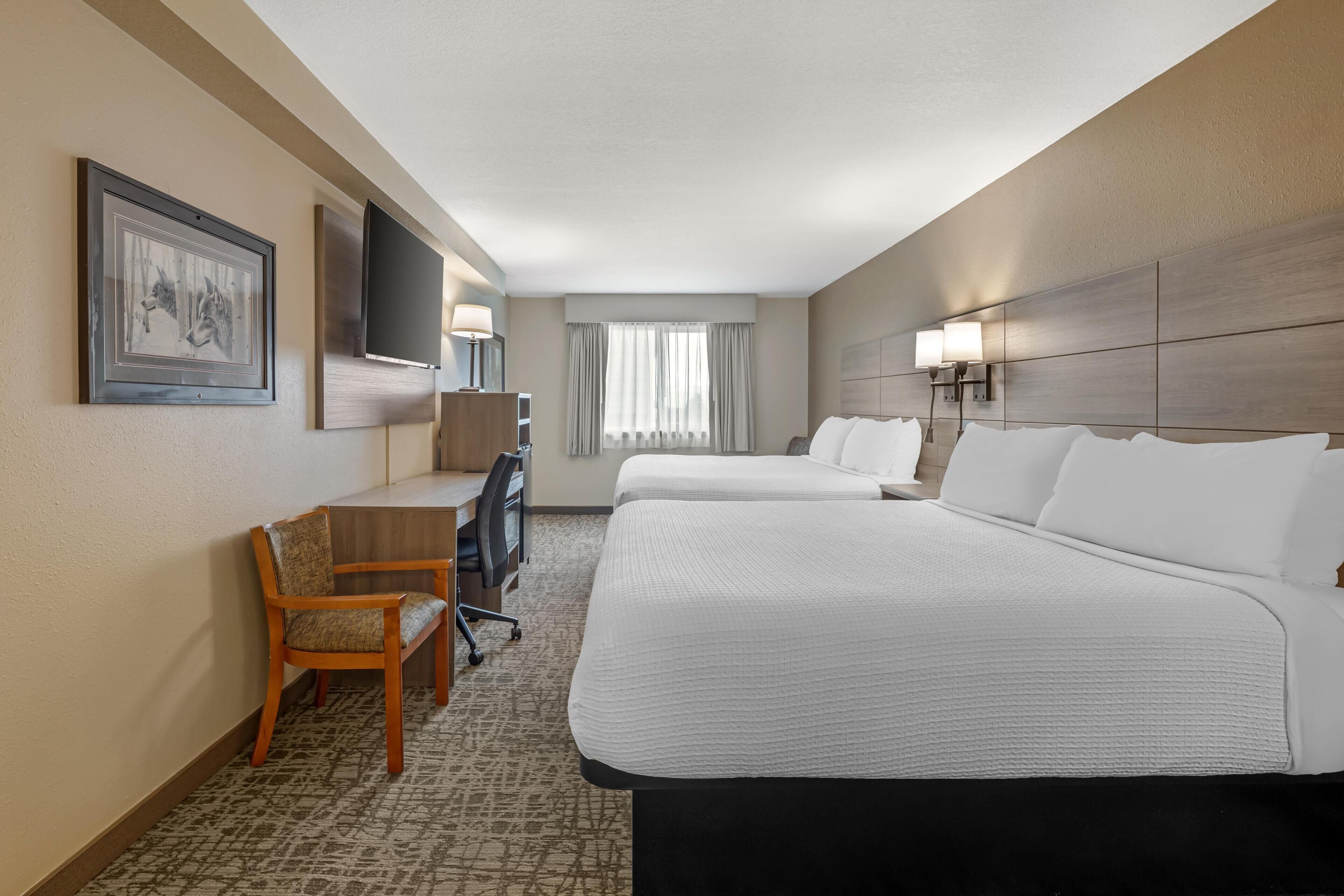 A hotel room with a bed, desk, chair, and a television.