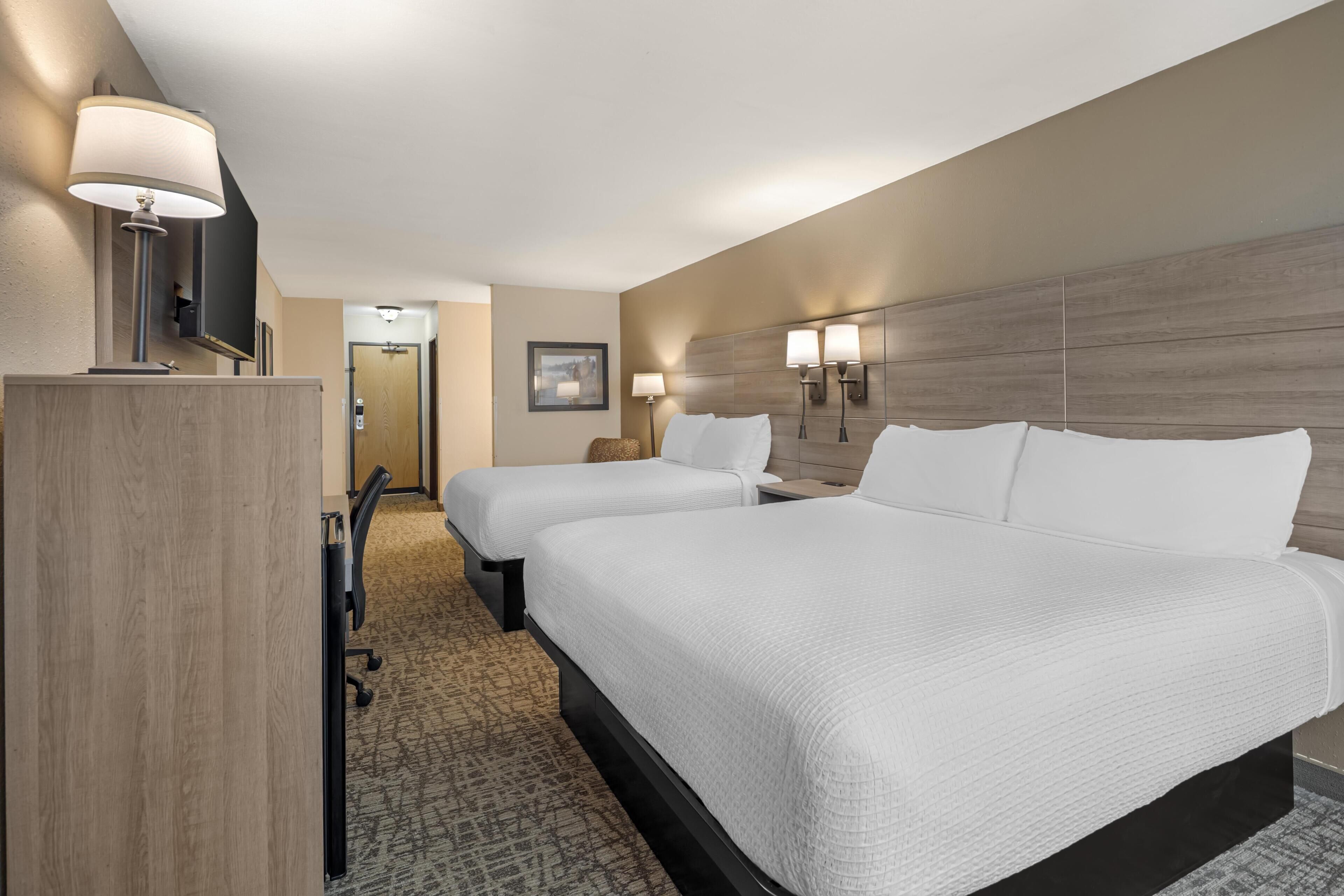 A hotel room with two beds, a desk, a chair, a TV, and a door leading to a bathroom.