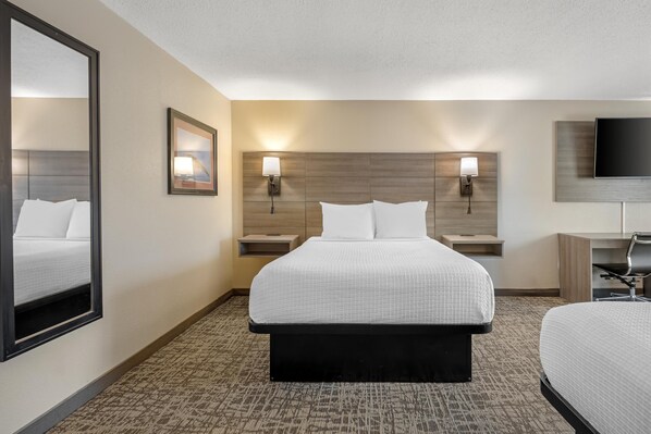 A hotel room with a large bed, two bedside tables with lamps, a flat-screen TV, and a large mirror.