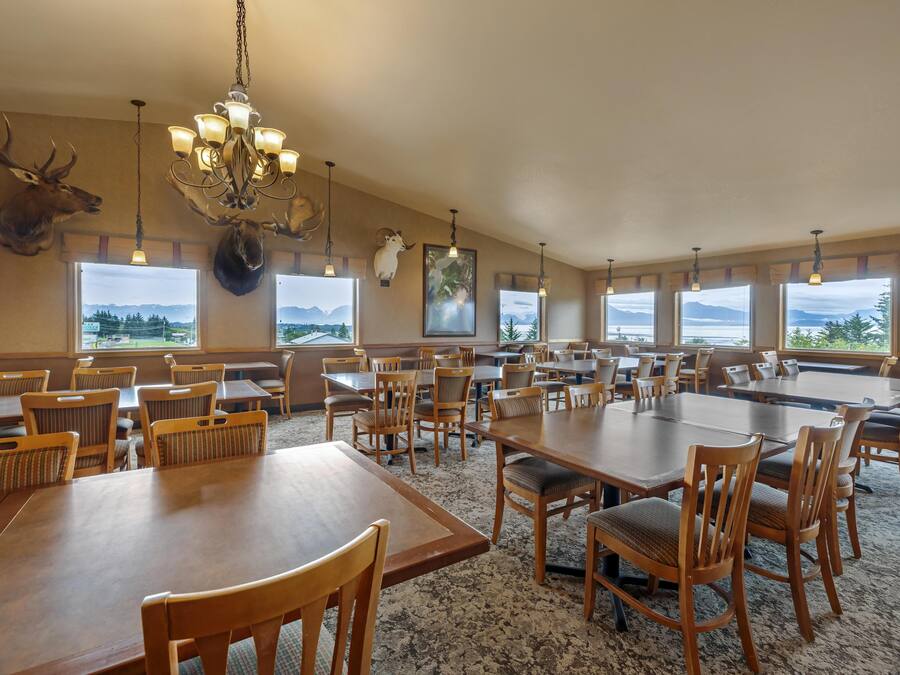 A spacious dining area with multiple tables and chairs, large windows offering views of mountains, and a chandelier with light fixtures.