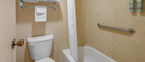 A bathroom with a toilet, a shower, and a bathtub. There are two bottles of shampoo on the wall.