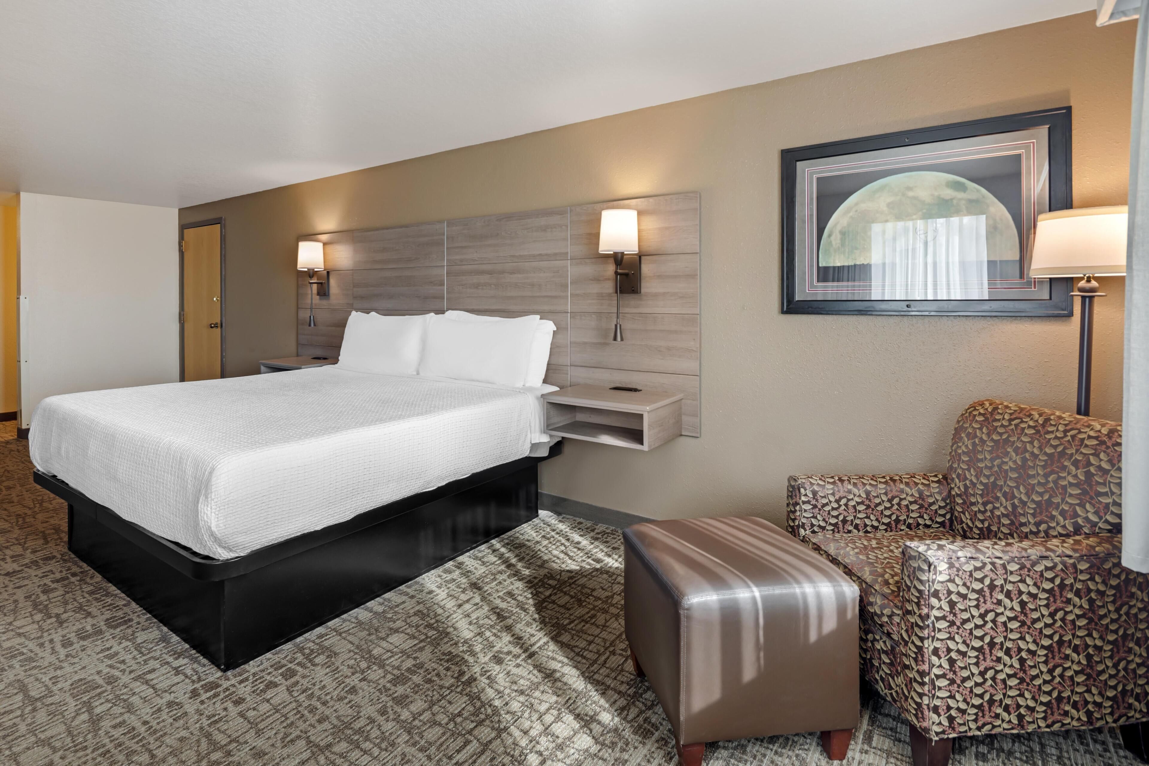 A hotel room with a bed, bedside tables, a chair, and a wall-mounted lamp.