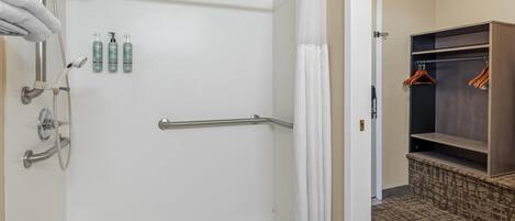 Een inloopdouche met een handgreep, een witte douchegordijn en verzorgingsproducten aan de muur.