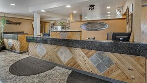 A reception desk with a herringbone wood and tile design, a reception area with a wooden wall and a decorative mirror, and a ceiling with recessed lighting. - Best Western Bidarka Inn (Homer)
