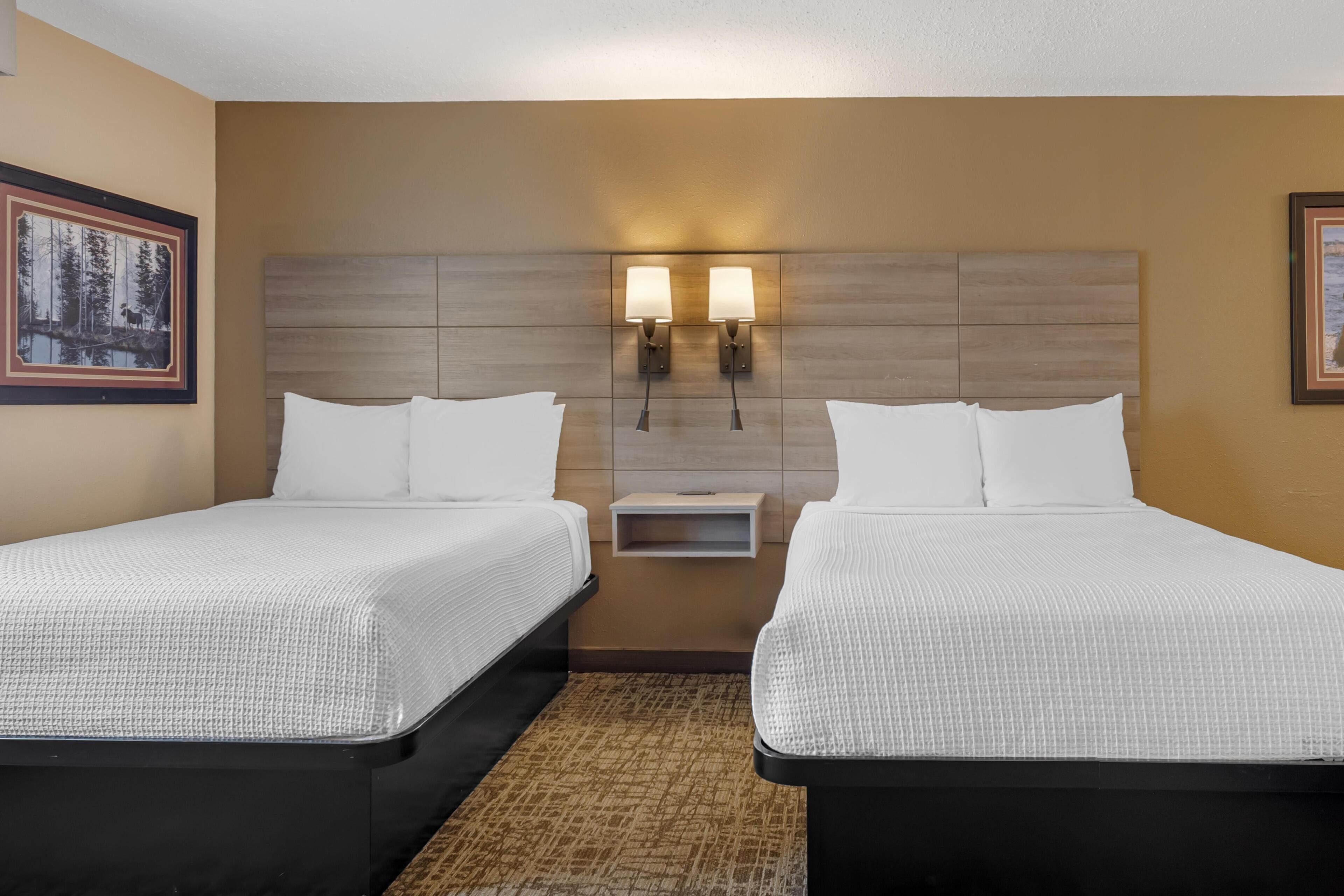 A hotel room with two single beds, a nightstand, and two wall-mounted lamps.