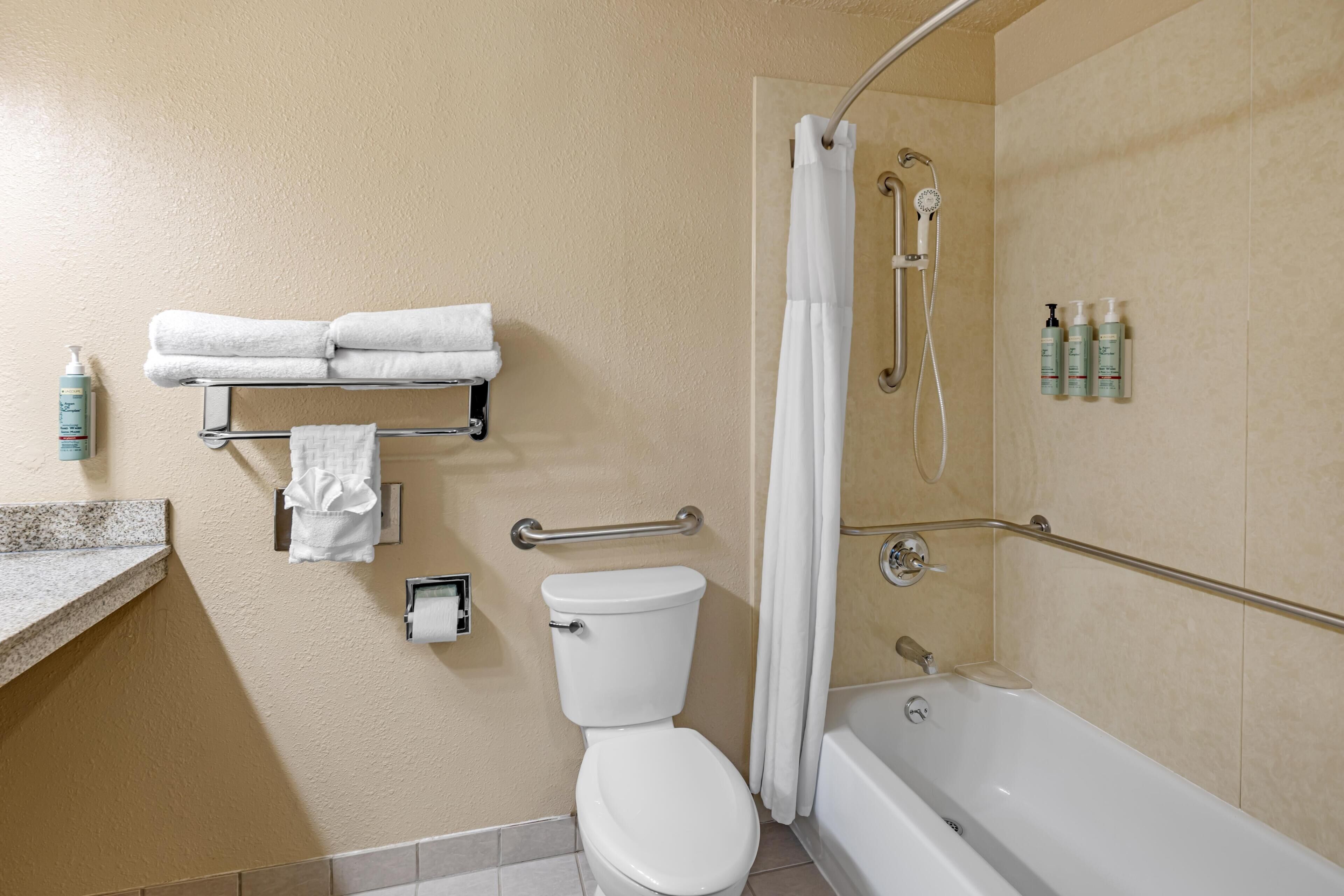 A bathroom with a toilet, a bathtub, a shower, and a towel rack with folded towels.