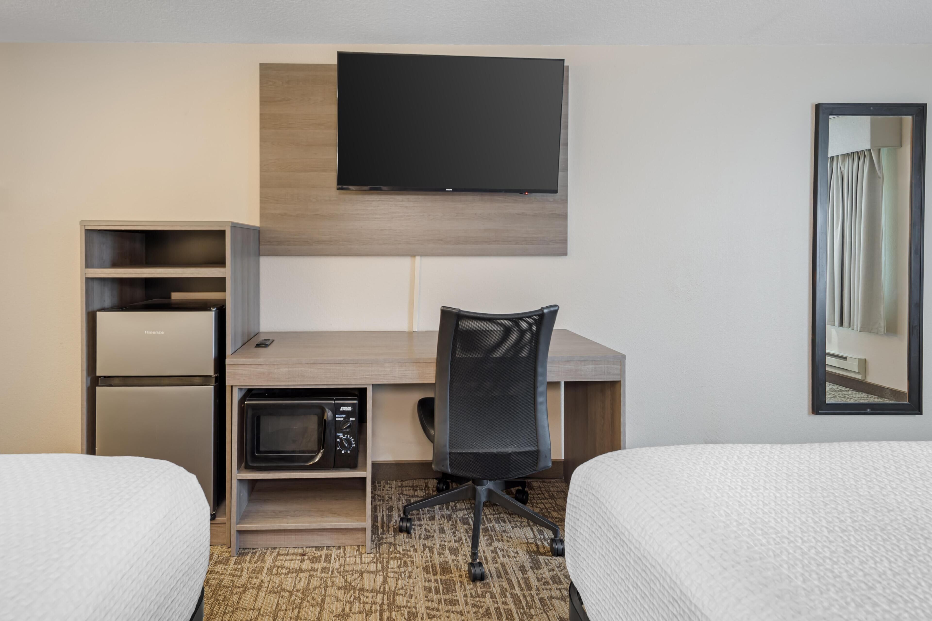 A hotel room with a bed, a desk with a chair, a television, a microwave, and a wardrobe.