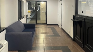 A hallway with a blue sofa, a tiled floor, a ceiling light, and a door with a sign.