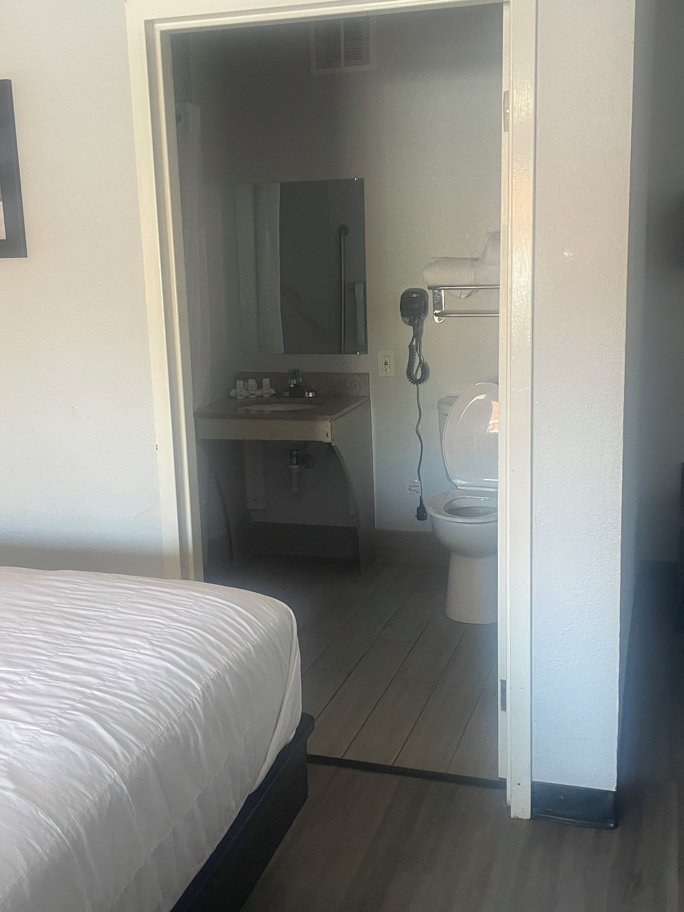 A hotel room with a bed, a bathroom with a sink, mirror, and toilet.