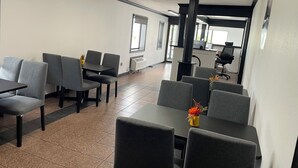 A conference room with grey chairs and tables, a large pillar, and a window with blinds.