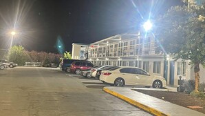 A parking lot with several cars parked in front of a building with multiple floors and balconies.